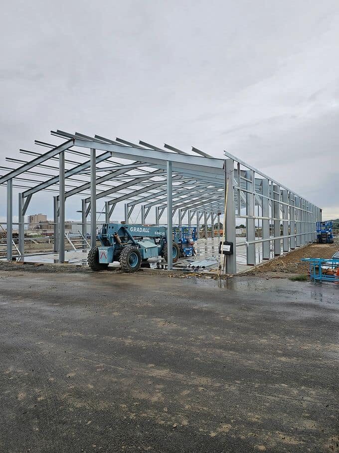 The steel frame of a large building standing on site during construction, with a telehandler alongside