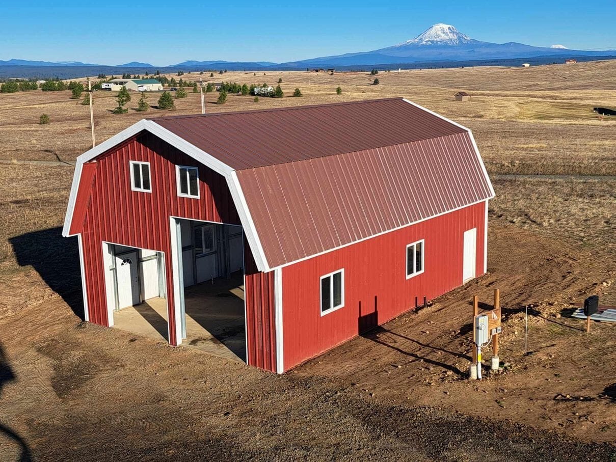 A red steel barn with white trim standing on open high-desert ground