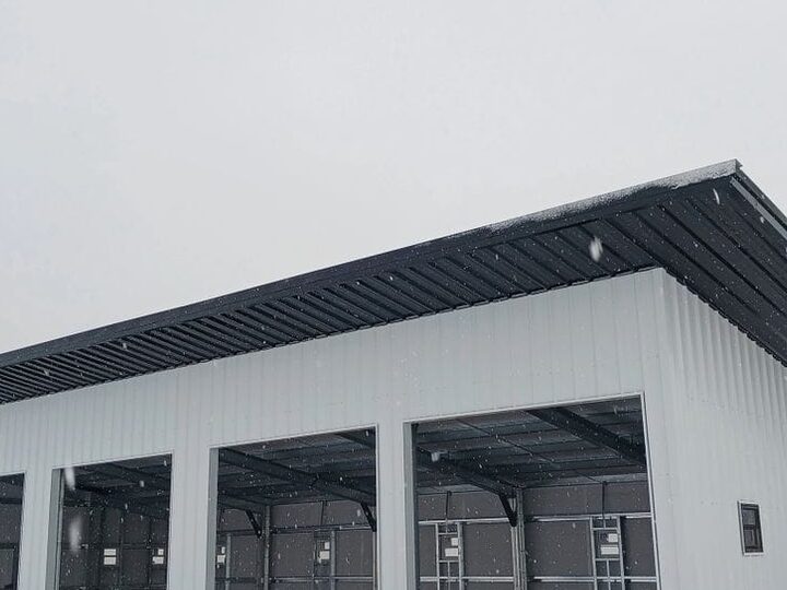 A white and charcoal multi-bay open-front steel equipment shed in winter