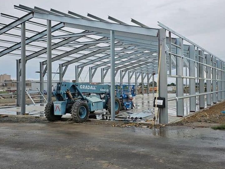 The steel frame of a large building standing on site during construction, with a telehandler alongside