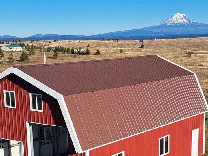A red steel barn with white trim standing on open high-desert ground